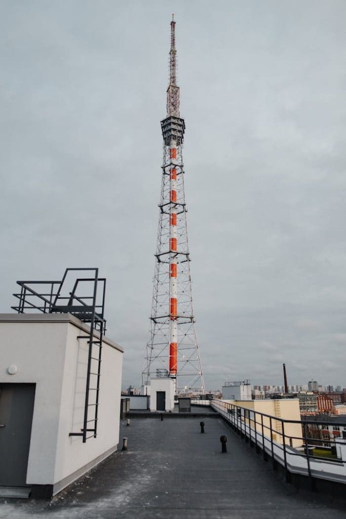 A towering telecommunication structure on a rooftop under a cloudy sky in an urban setting.